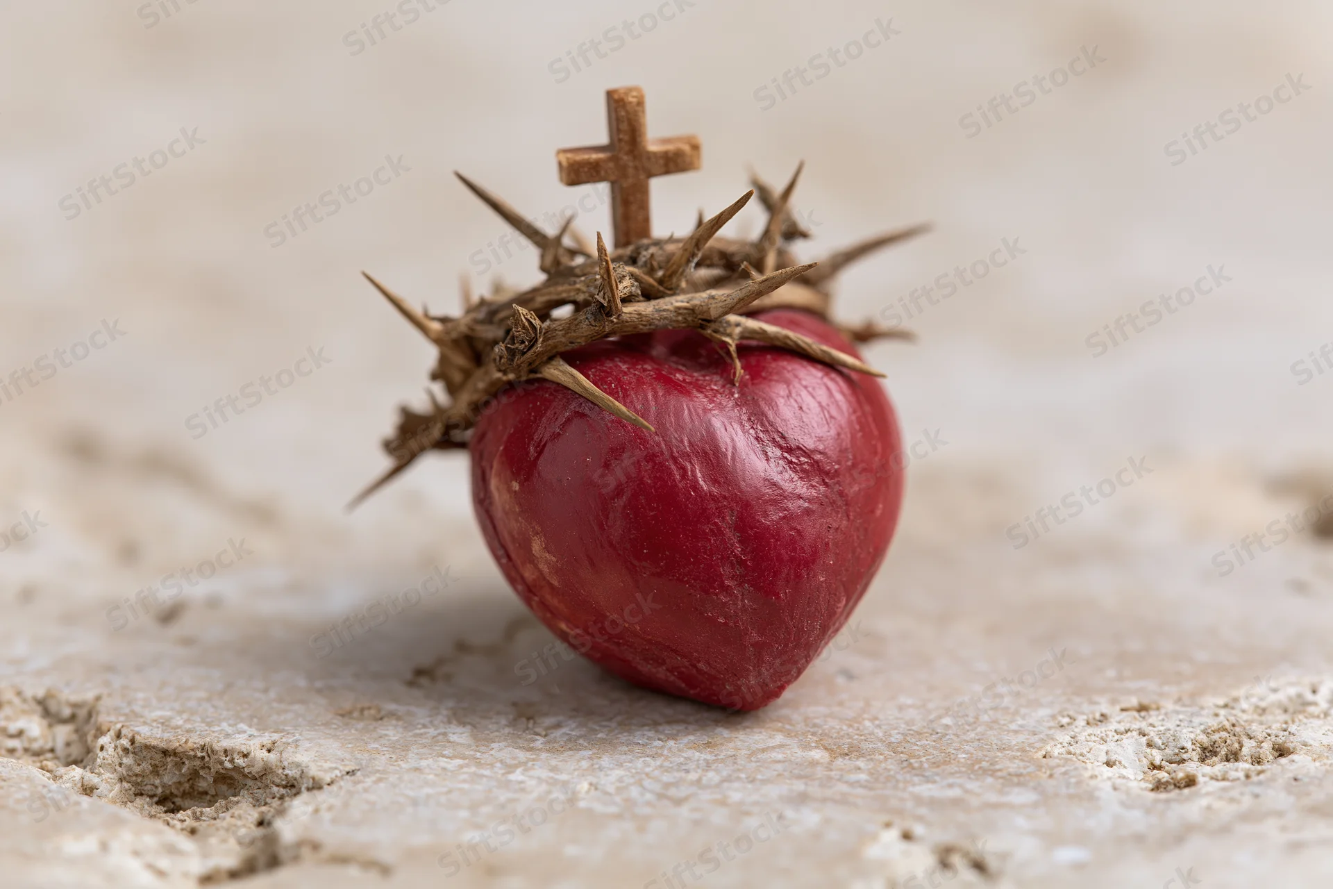 Red sculpted heart topped with crown of thorns and small cross resting on stone surface