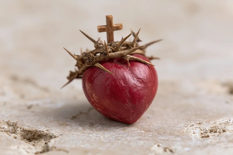 Red sculpted heart topped with crown of thorns and small cross resting on stone surface