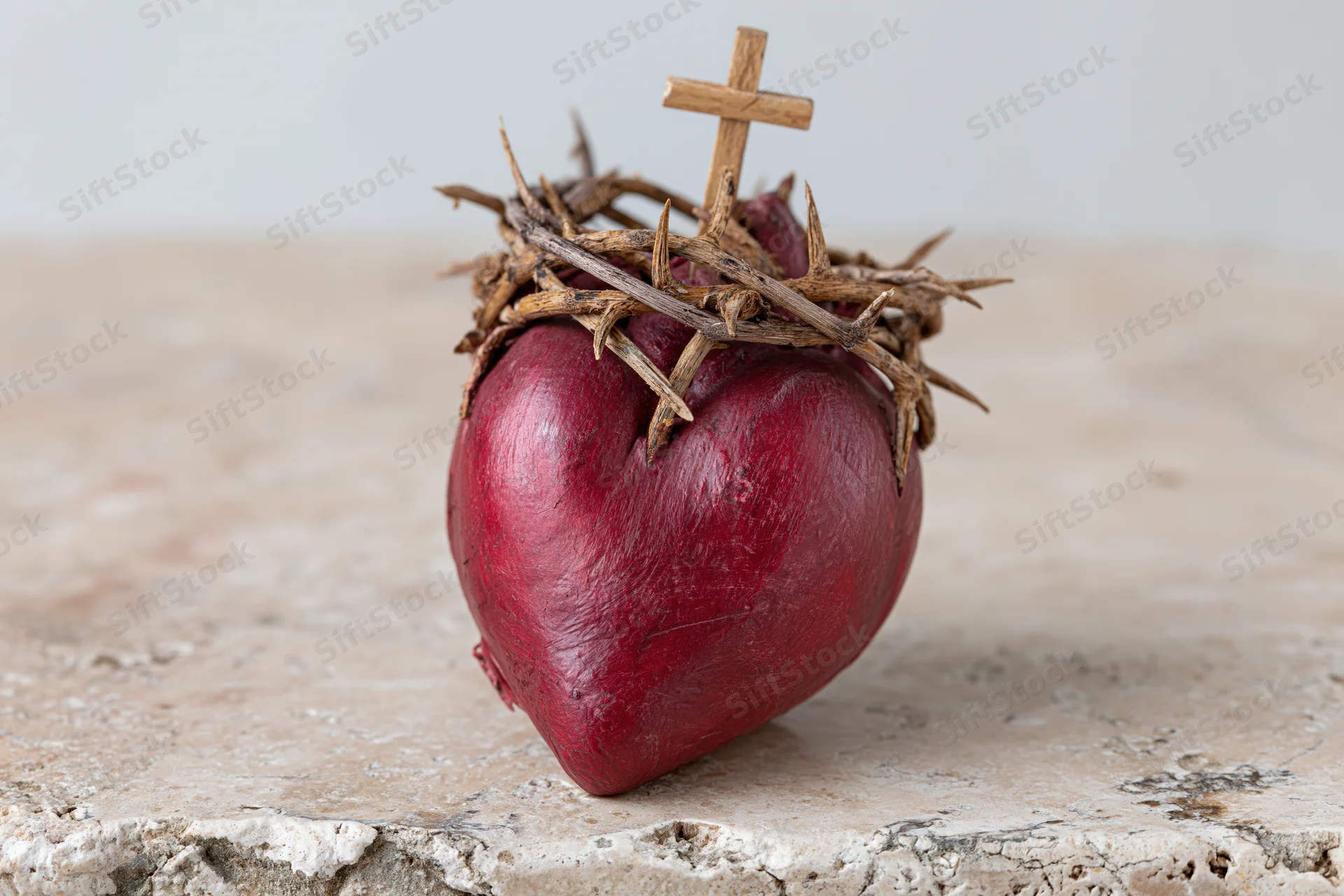 Red sculptural heart with crown of thorns and small cross on stone surface