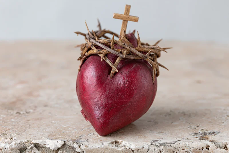 Red sculptural heart with crown of thorns and small cross on stone surface