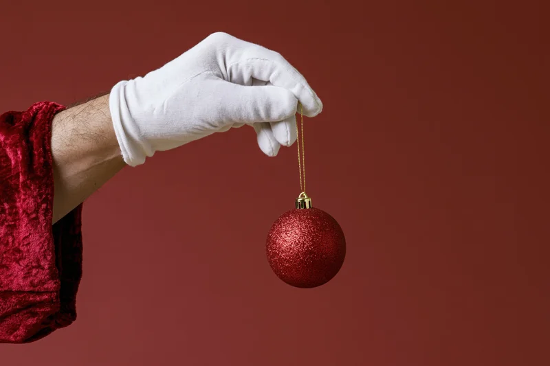 Santa's white-gloved hand holding a red glitter ornament against a red background
