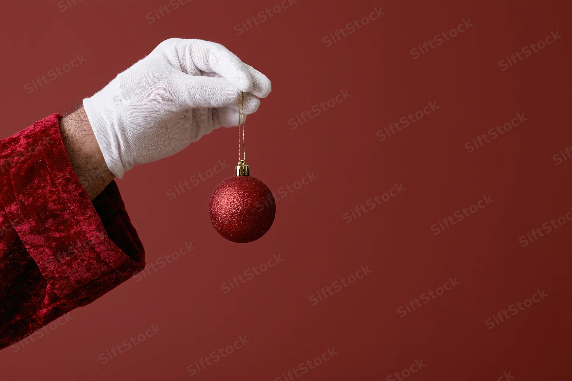 Santa's white-gloved hand holding a red glitter ornament against a red background
