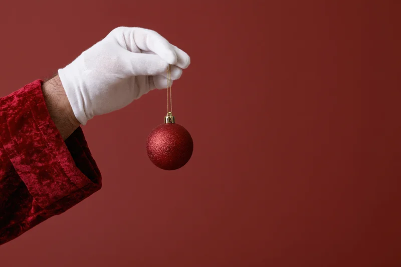 Santa's white-gloved hand holding a red glitter ornament against a red background