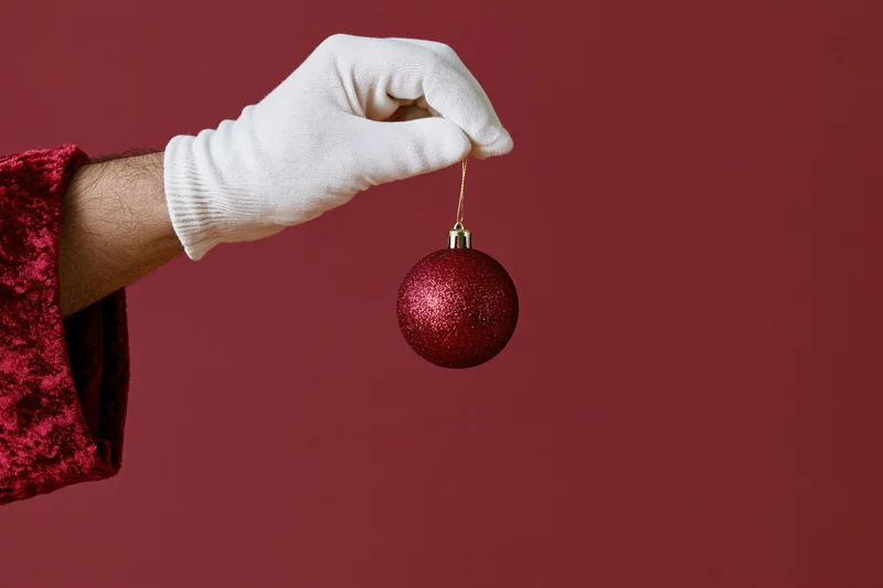 Santa's white-gloved hand holding a red glitter ornament against a red background