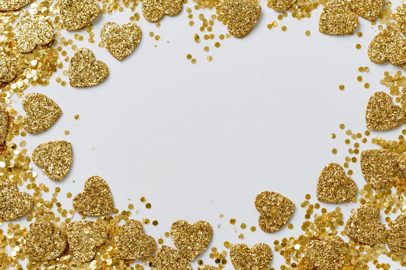 Gold glitter hearts and round confetti scattered in a frame on white surface with copyspace