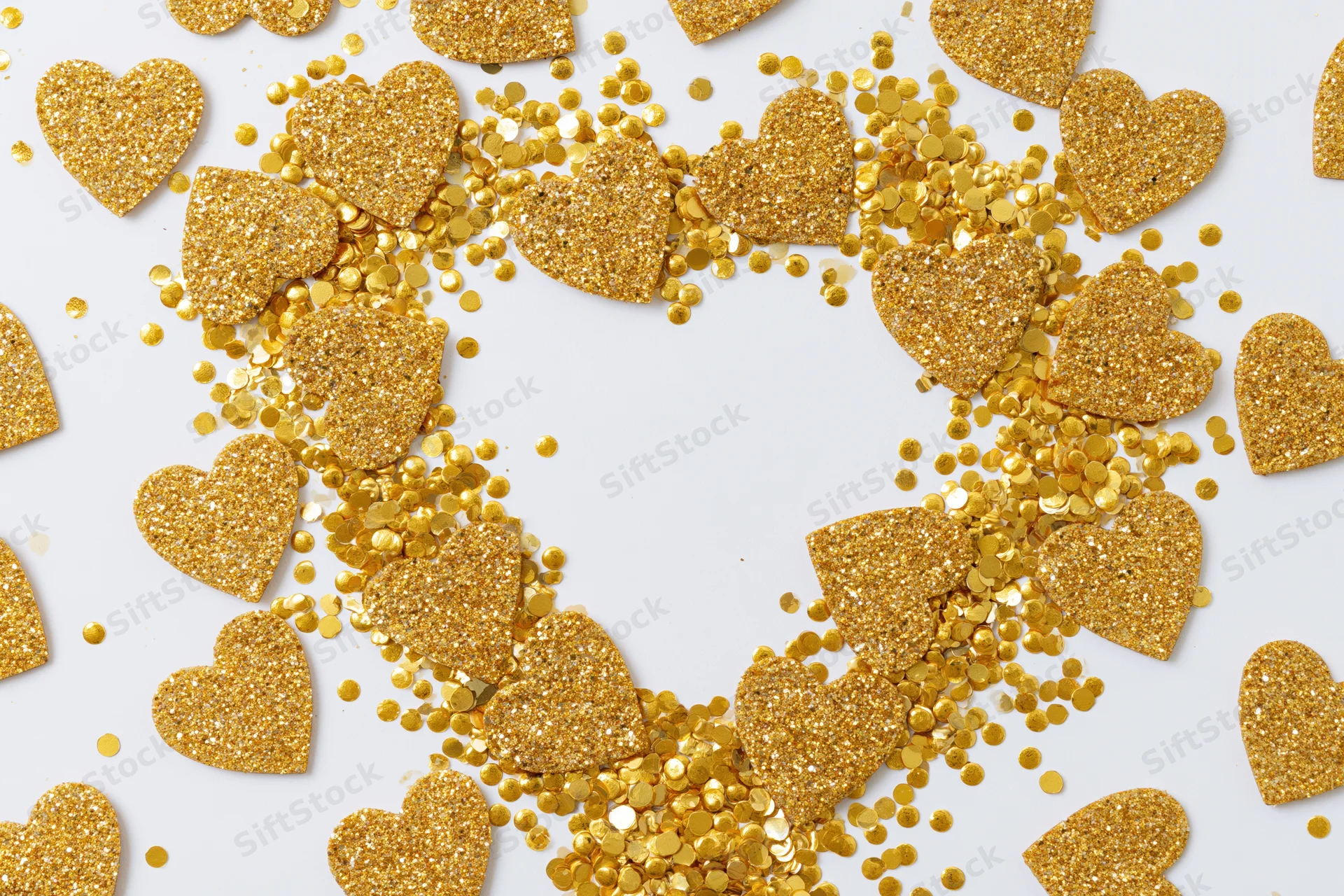 Gold glitter hearts and round confetti scattered on white surface forming a heart shape with copyspace in center