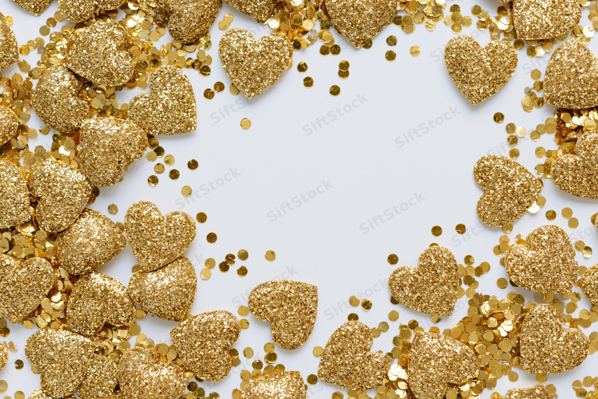 Gold glitter hearts and round confetti arranged in a frame on white background with copyspace