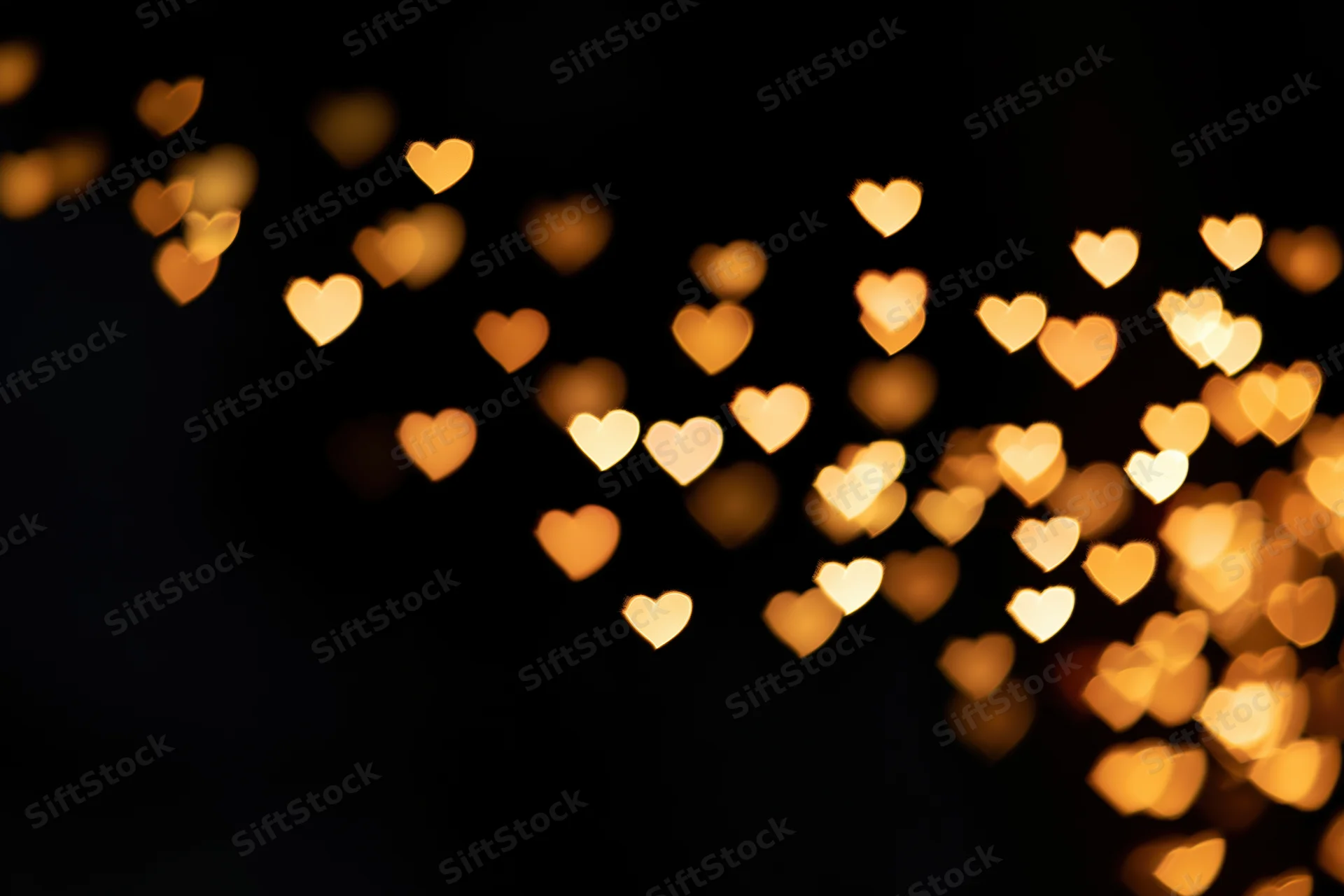 Heart-shaped bokeh lights scattered across a dark background with soft glow and copyspace on the left