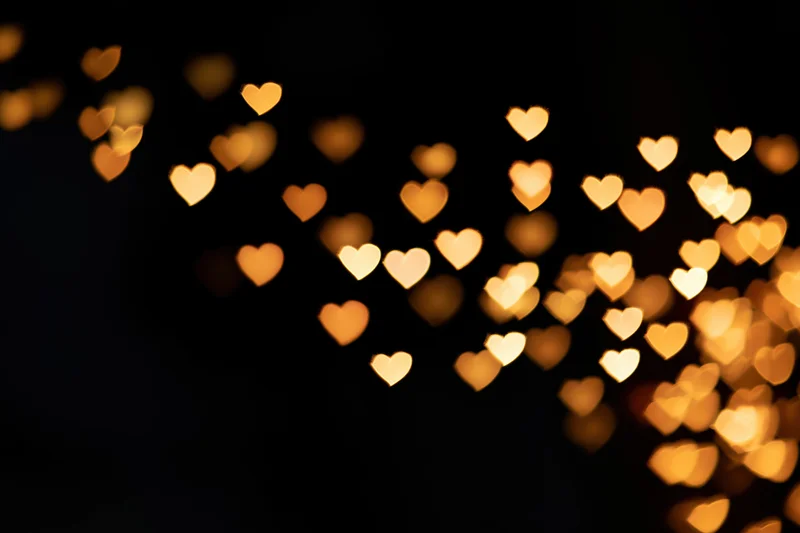 Heart-shaped bokeh lights scattered across a dark background with soft glow and copyspace on the left