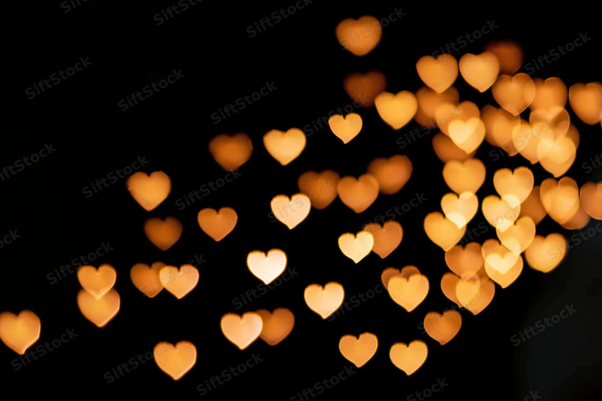 Heart-shaped bokeh lights scattered across a dark background with soft golden glow