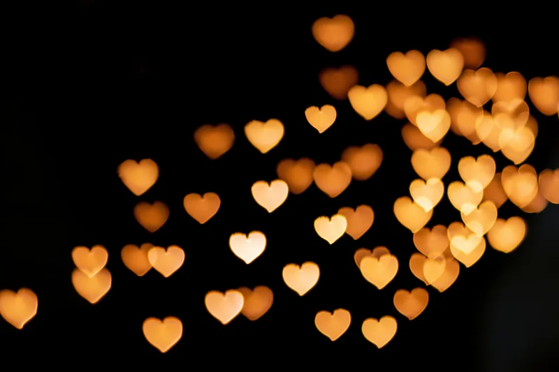 Heart-shaped bokeh lights scattered across a dark background with soft golden glow