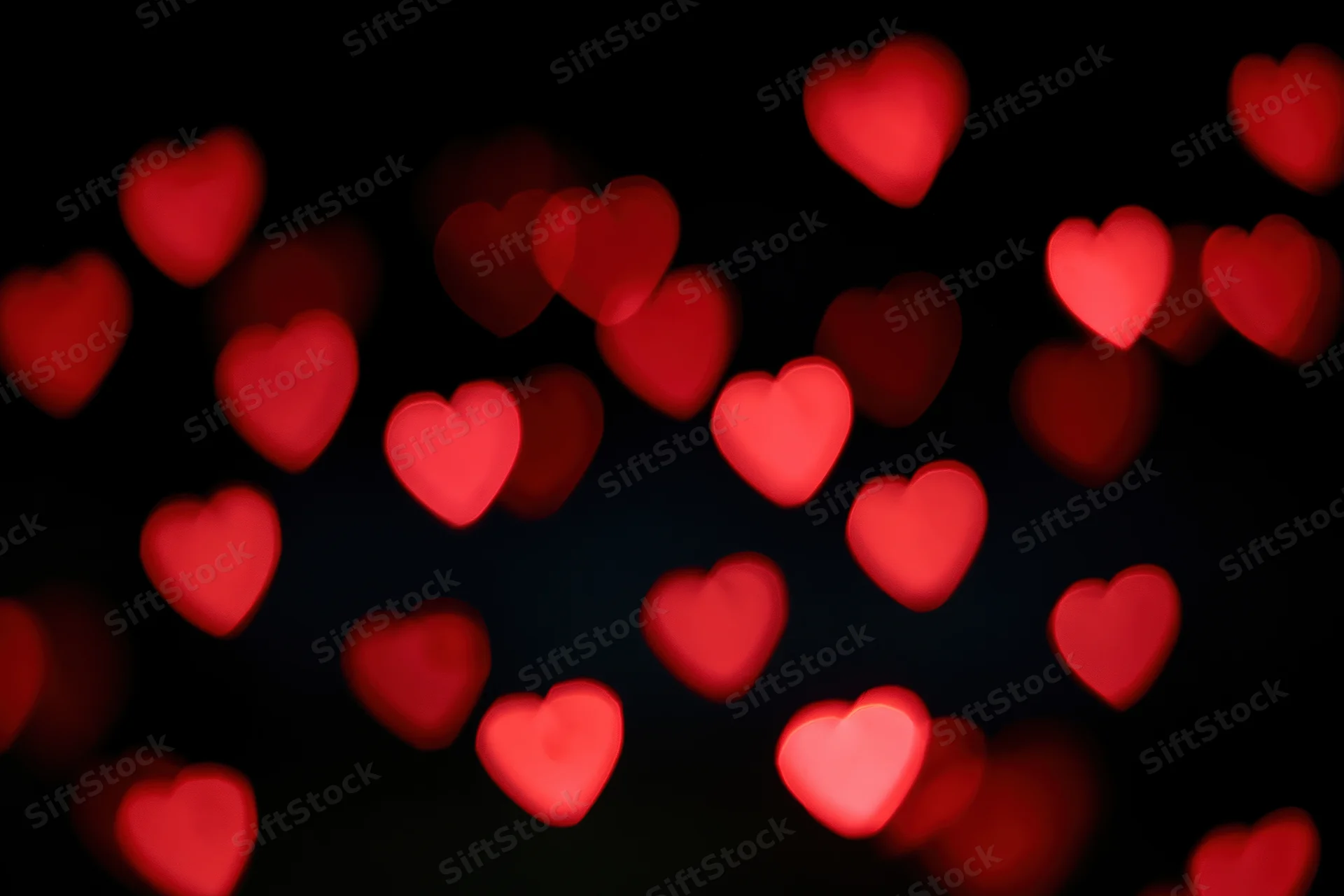 Scattered red heart-shaped bokeh lights floating against a dark background