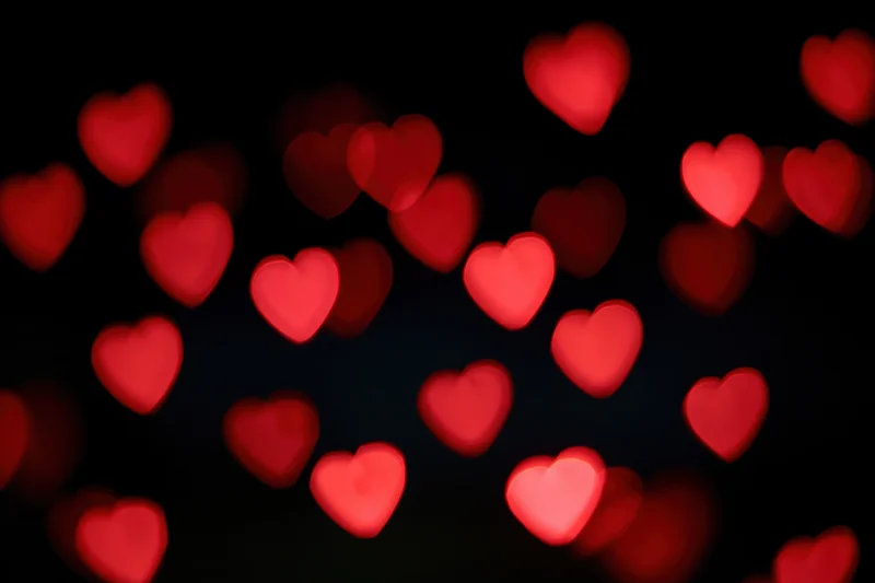 Scattered red heart-shaped bokeh lights floating against a dark background