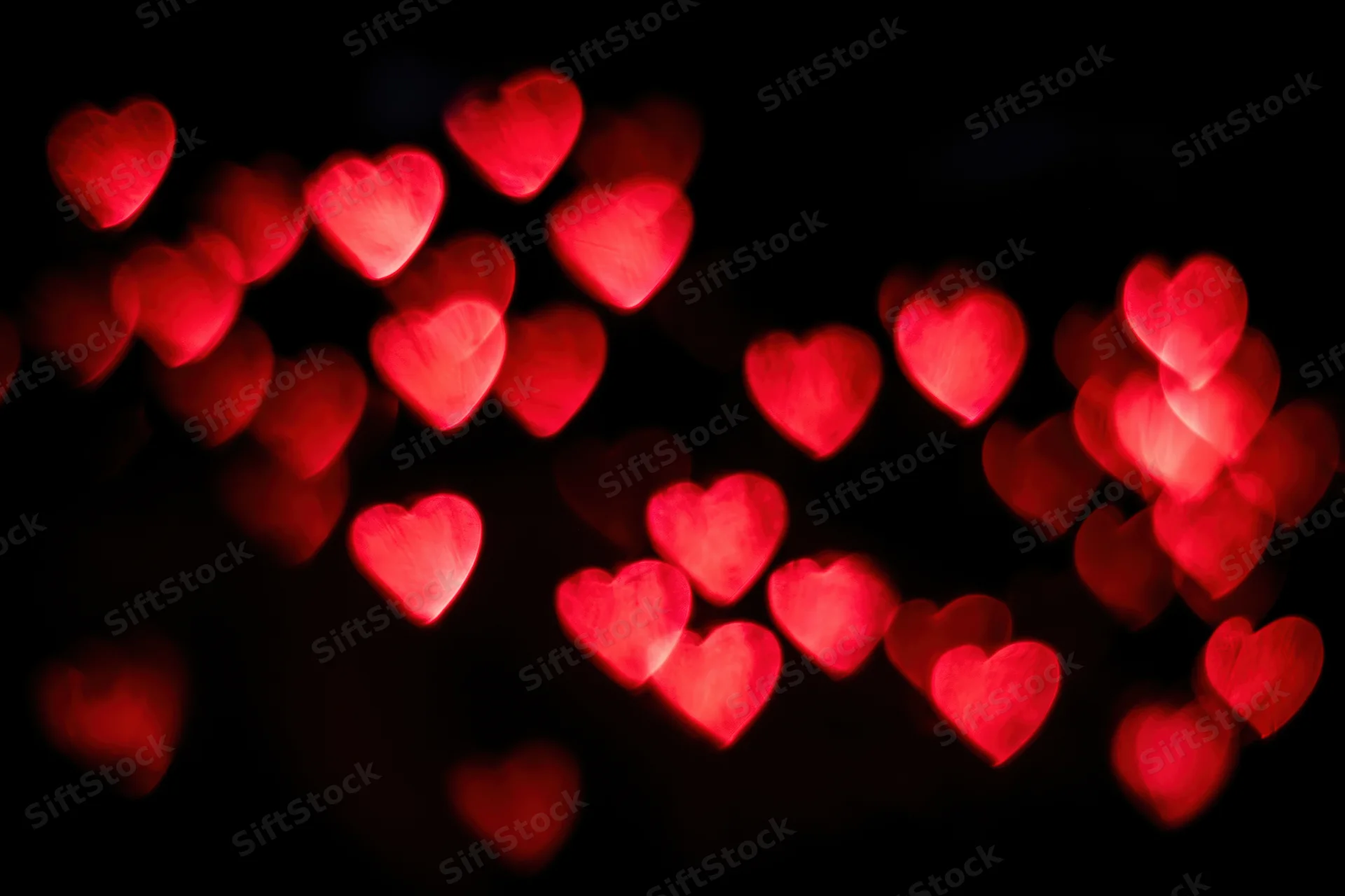 Red heart-shaped bokeh lights scattered against a dark background
