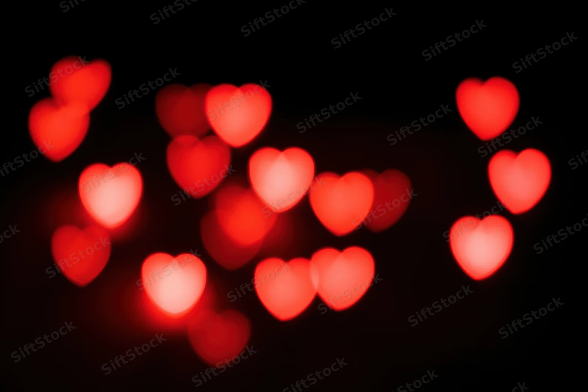 Scattered red heart-shaped bokeh lights floating against a black background