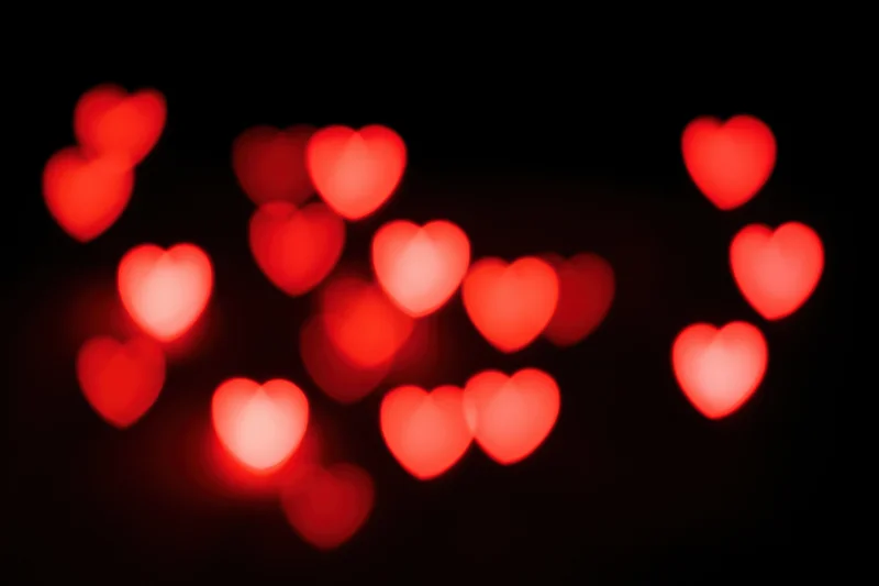 Scattered red heart-shaped bokeh lights floating against a black background