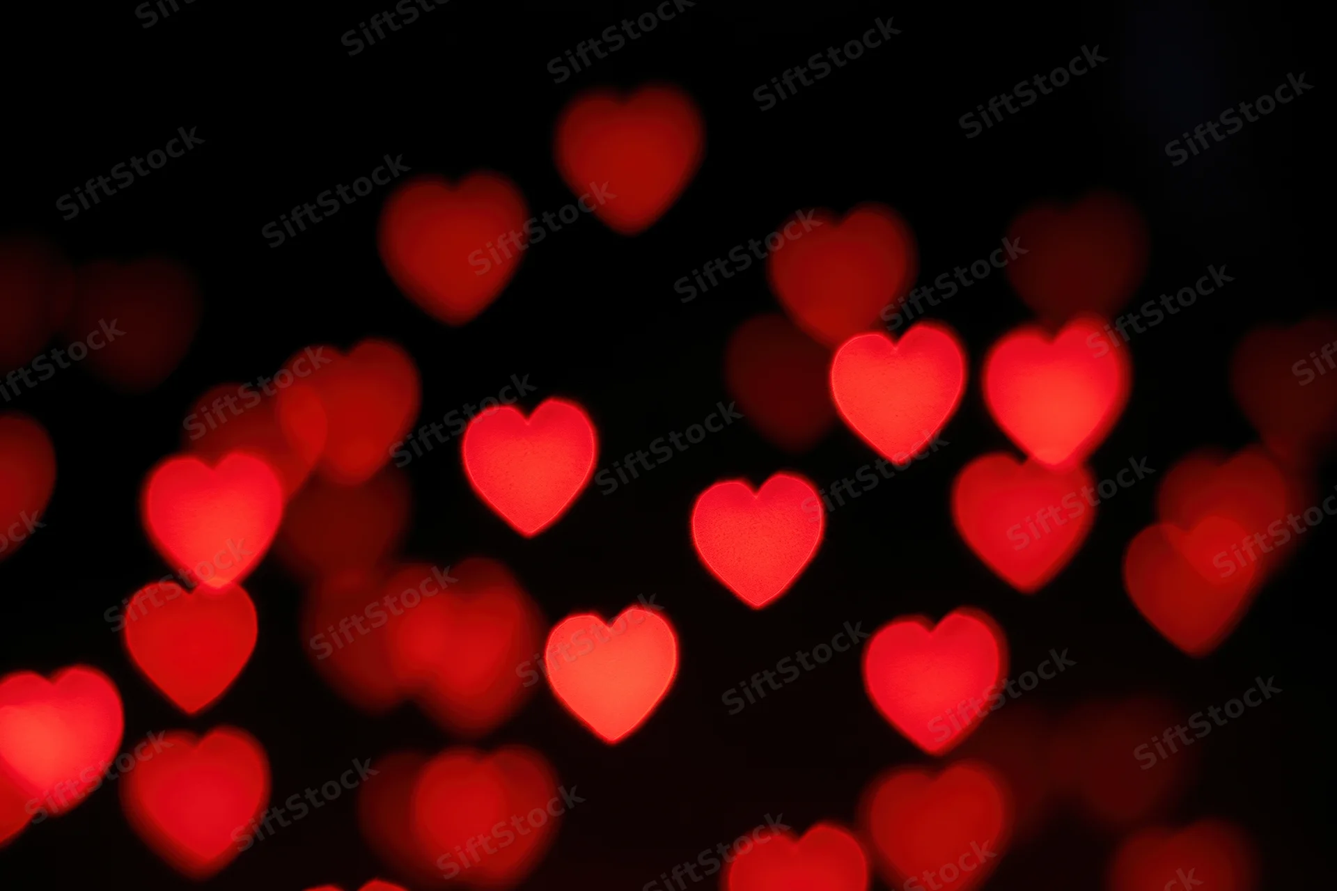 Red heart-shaped bokeh lights scattered against a dark background