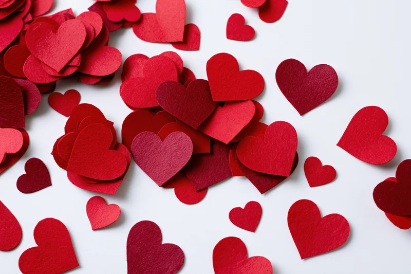 Scattered red paper hearts on white surface