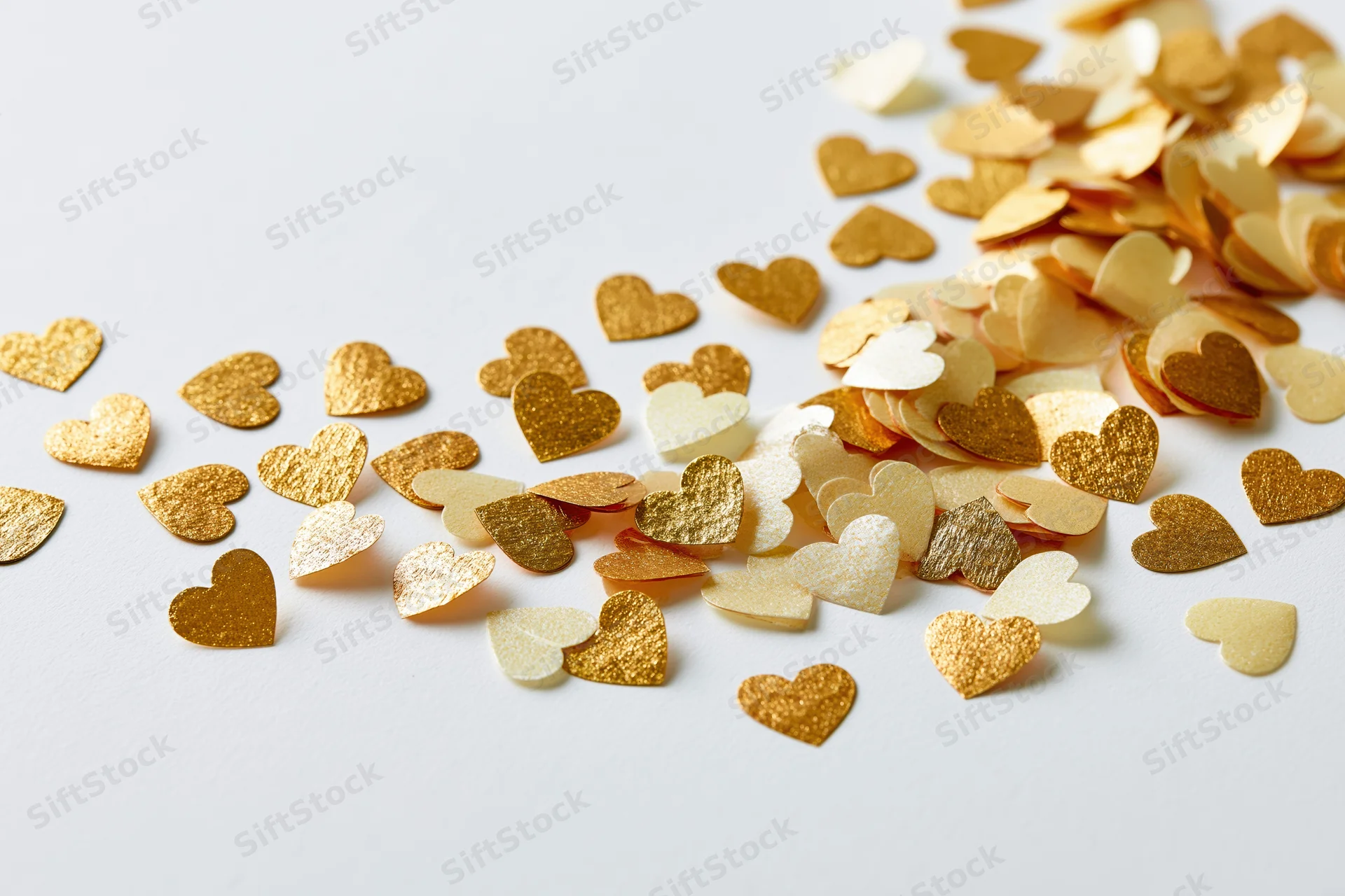 Scattered gold and pale yellow heart-shaped confetti on a white surface