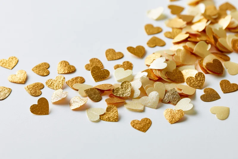 Scattered gold and pale yellow heart-shaped confetti on a white surface