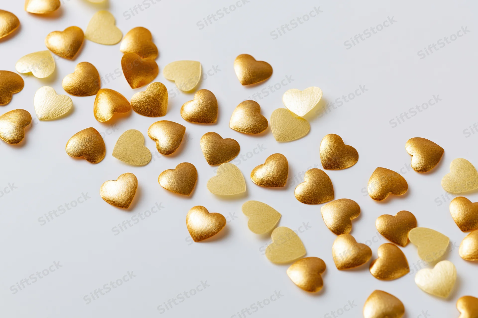 Scattered gold and pale yellow heart-shaped confetti on a white surface