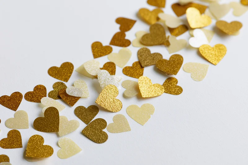 Scattered gold and pale yellow heart-shaped confetti on white surface
