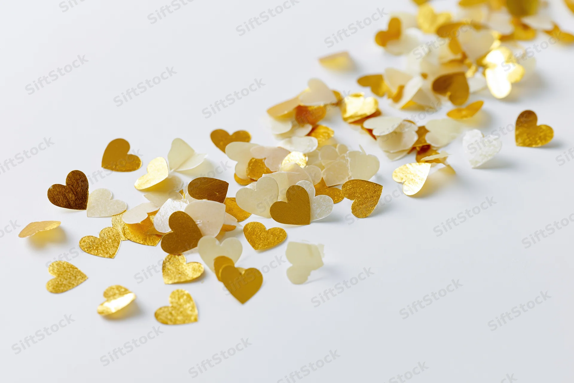 Scattered gold and pale yellow heart-shaped confetti on a white surface