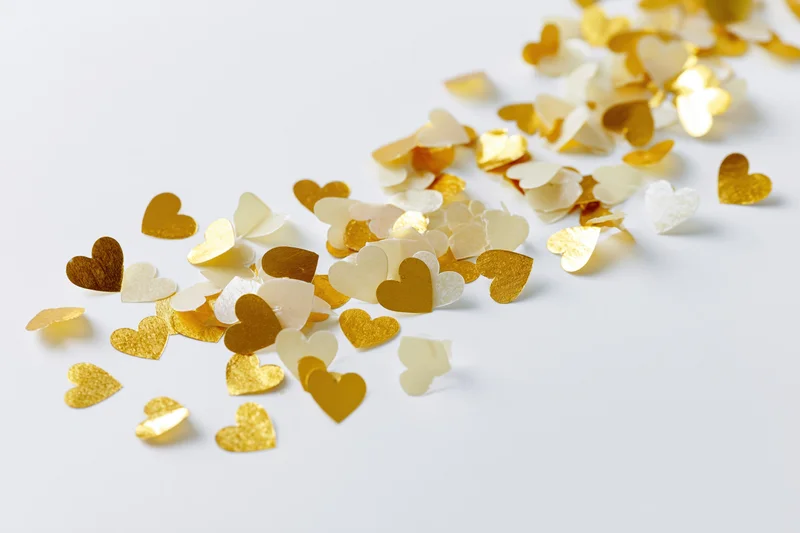 Scattered gold and pale yellow heart-shaped confetti on a white surface
