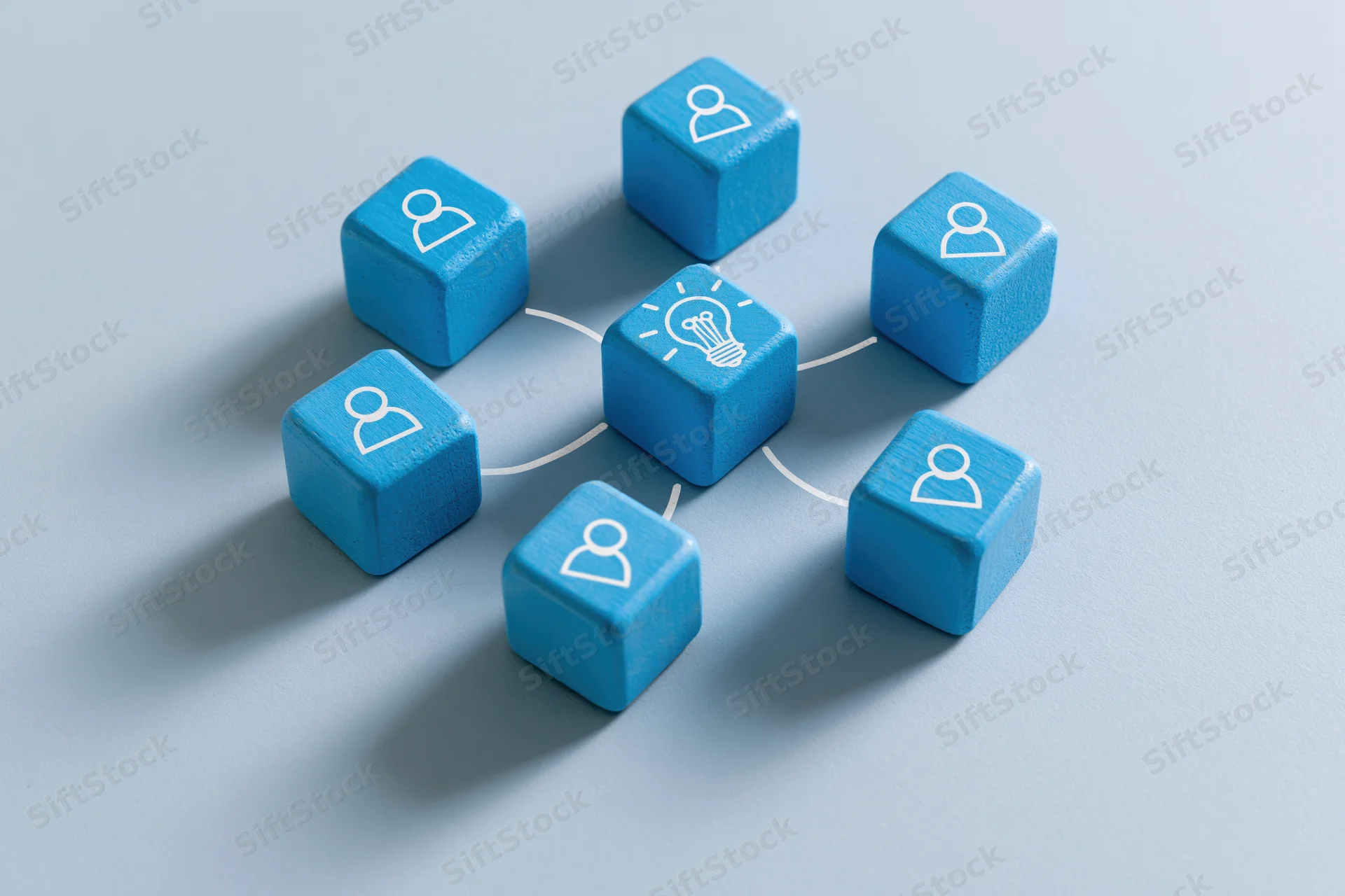 Blue wooden cubes with person and lightbulb icons connected by lines on a pale blue surface