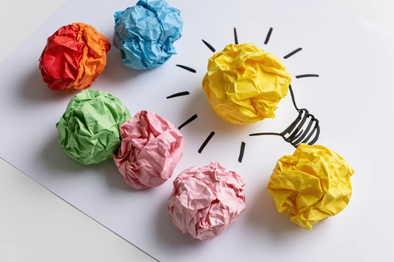 Crumpled colorful paper balls arranged around a hand-drawn lightbulb on white surface