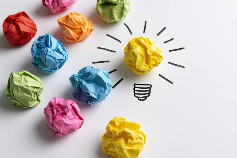 Crumpled colorful paper balls arranged around a hand-drawn lightbulb on white surface
