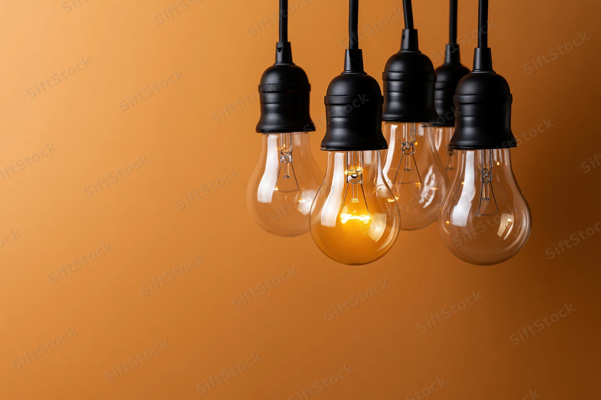 Several incandescent light bulbs hanging from black sockets against an orange gradient background with one illuminated and copyspace on the left