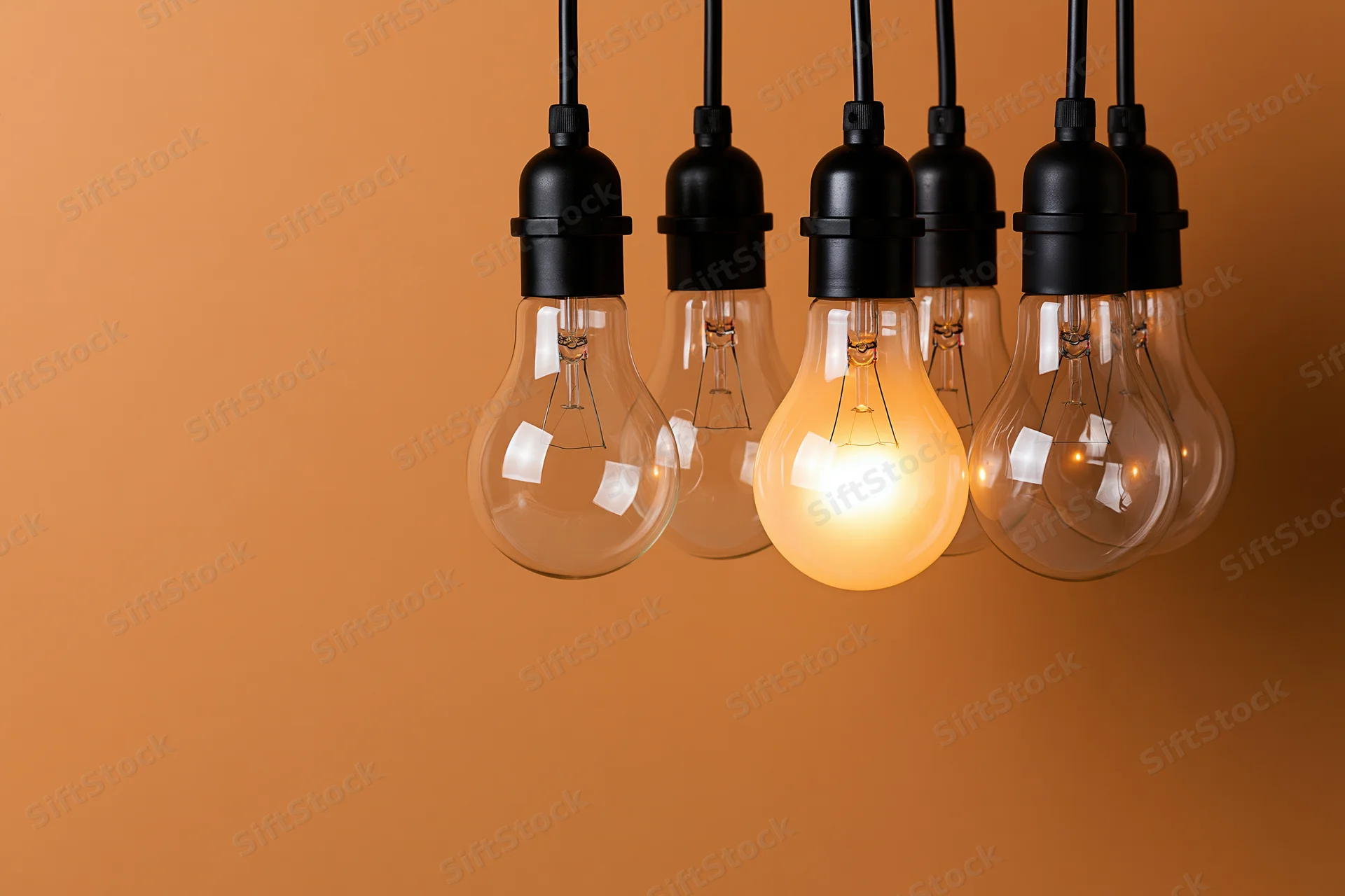 Several incandescent light bulbs hanging from black sockets against an orange background with one illuminated