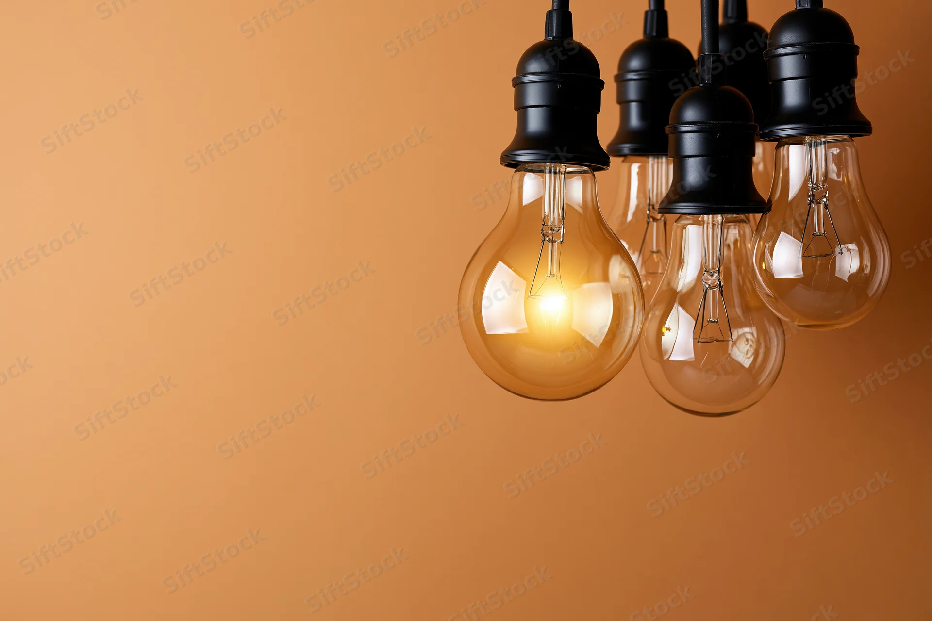 Several incandescent light bulbs hanging from black sockets against an orange background with copyspace on the left