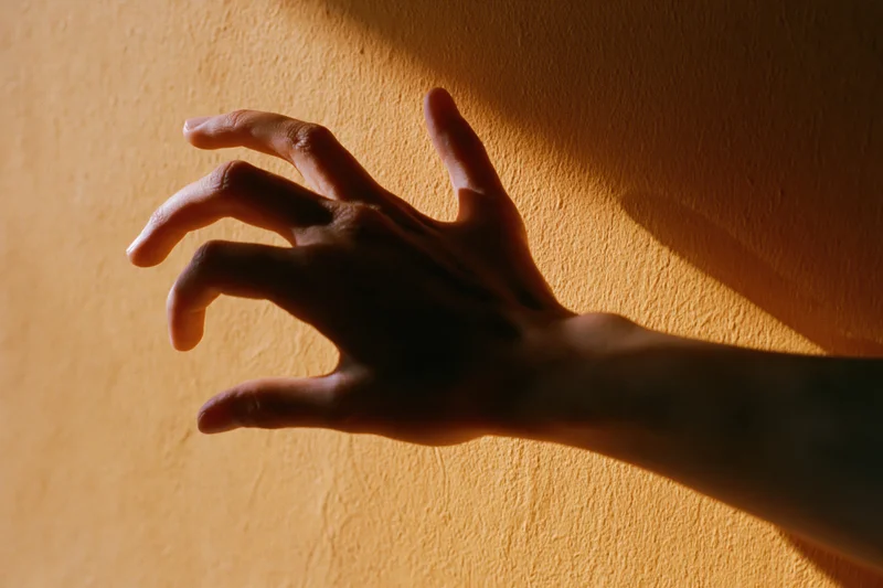 Hand reaching forward casting shadow on textured orange wall