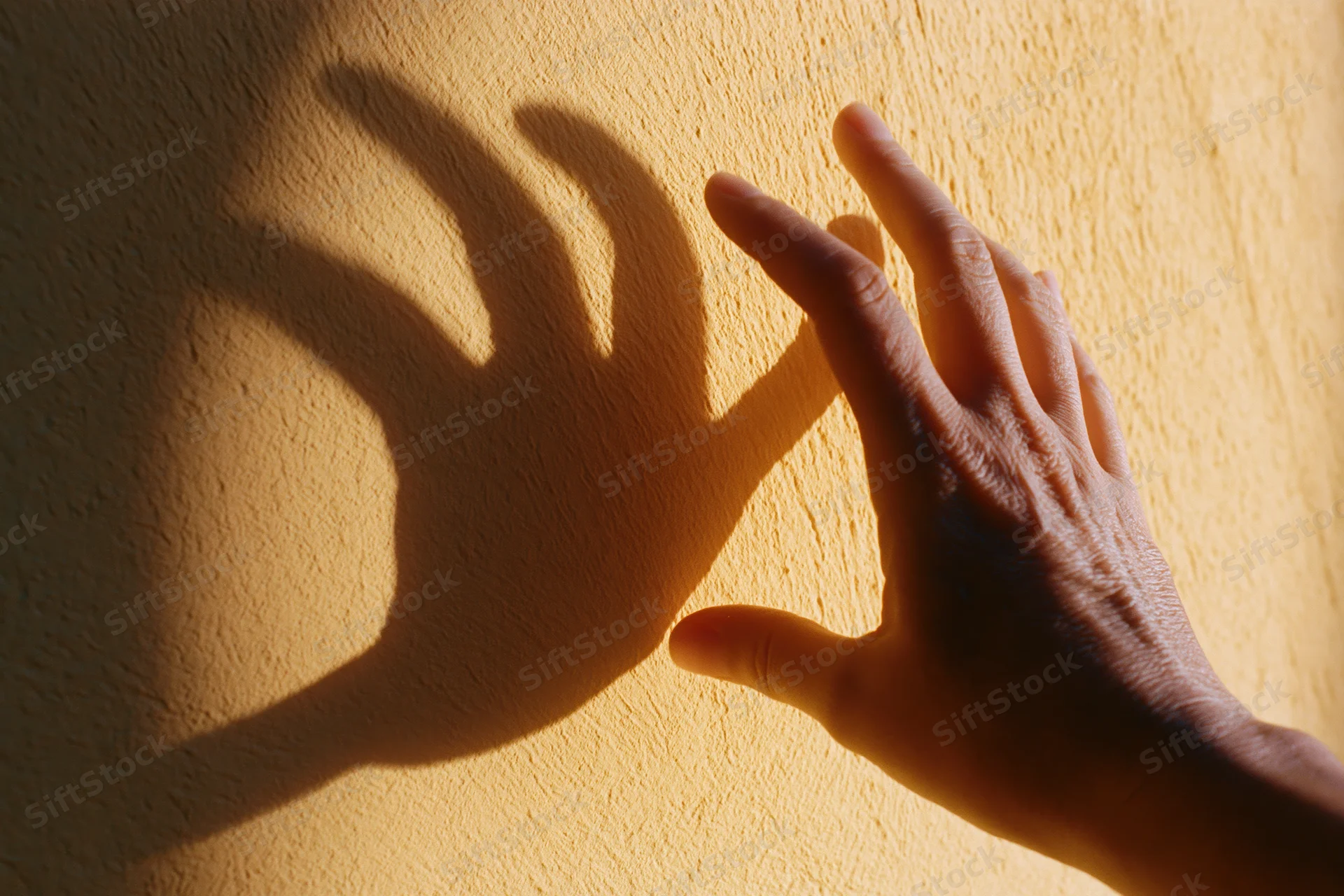 Hand reaching toward a textured plaster wall casting a shadow in warm light