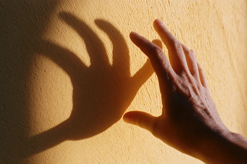 Hand reaching toward a textured plaster wall casting a shadow in warm light