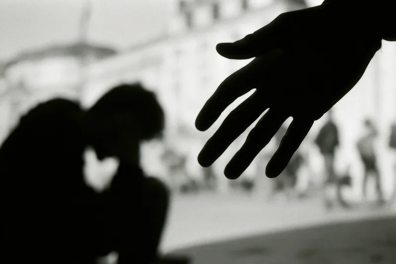 Silhouette of a hunched young person with a reaching hand in an urban setting