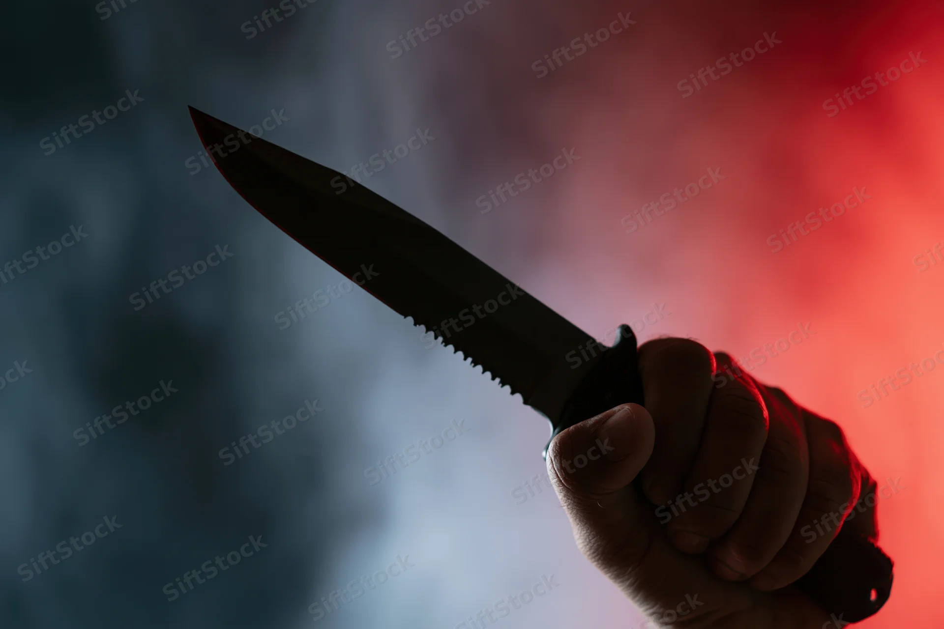 Hand gripping a tactical serrated knife raised against a smoky red and blue background