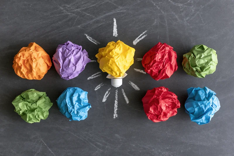 Crumpled colorful paper balls arranged around a chalk-drawn lightbulb on a blackboard surface