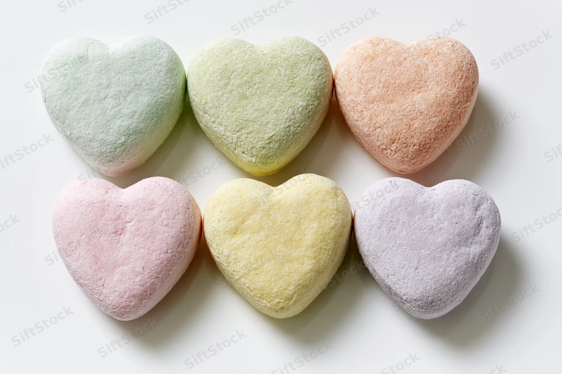 Six pastel heart-shaped candies arranged in two rows on a white surface
