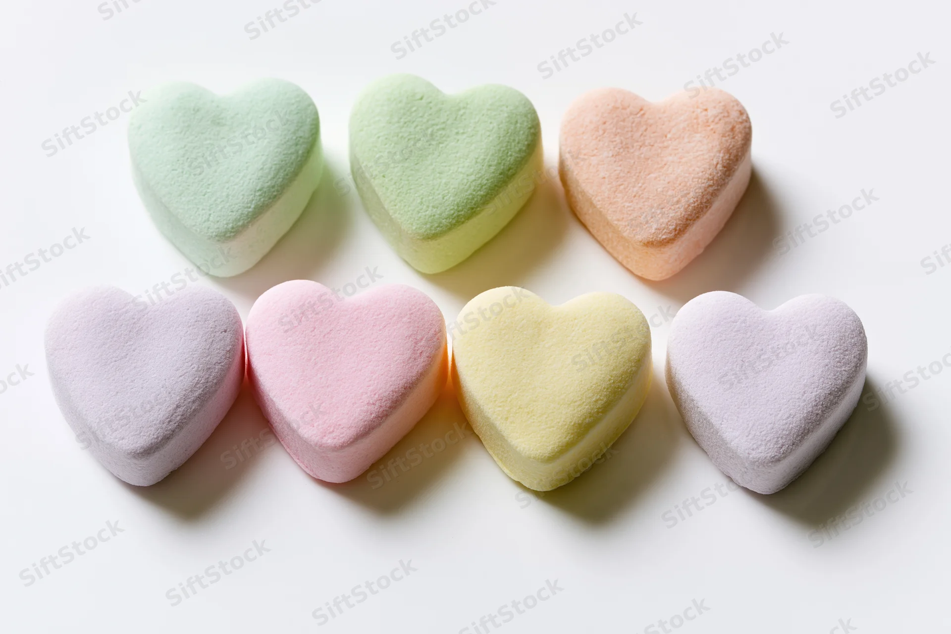 Six pastel heart-shaped candies arranged in two rows on a white surface