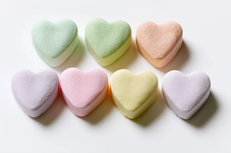 Six pastel heart-shaped candies arranged in two rows on a white surface