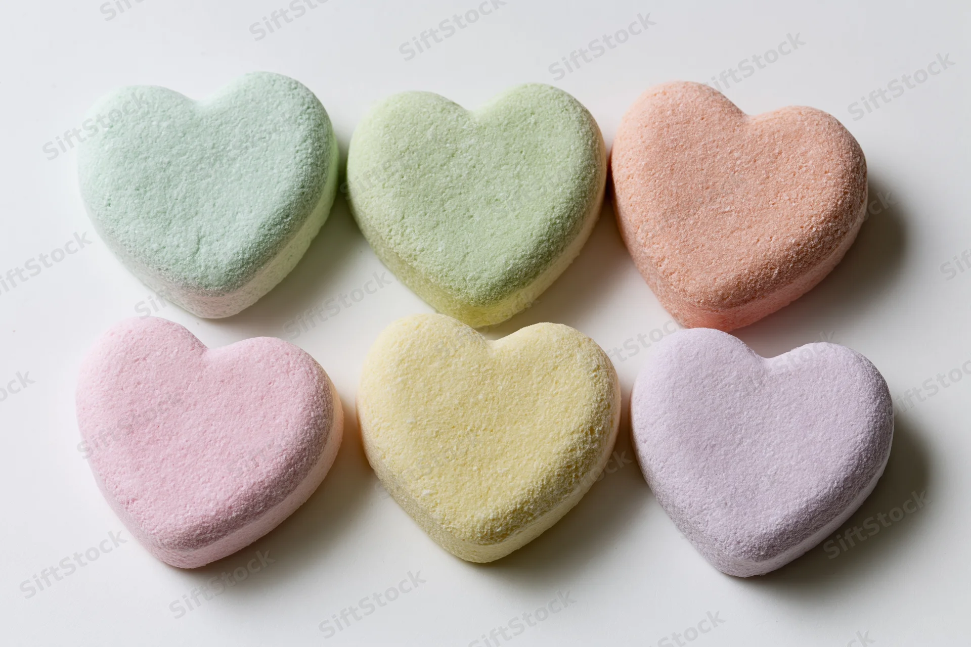 Six pastel heart-shaped candies arranged in two rows on a white surface