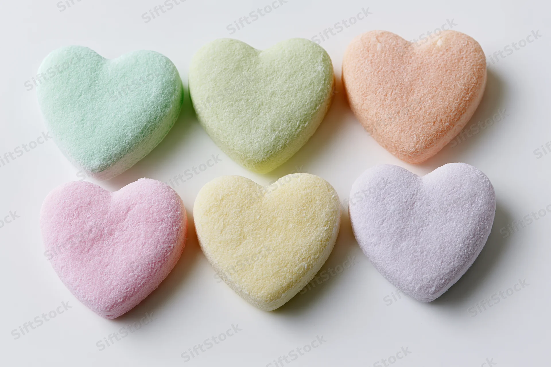 Six pastel heart-shaped candies arranged in two rows on a white surface