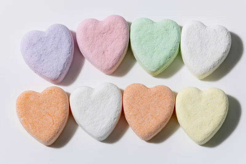 Eight pastel heart-shaped candies arranged in two rows on a white surface