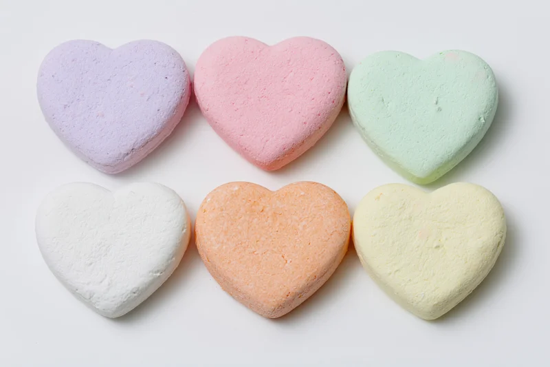 Six pastel heart-shaped candies arranged in two rows on white background