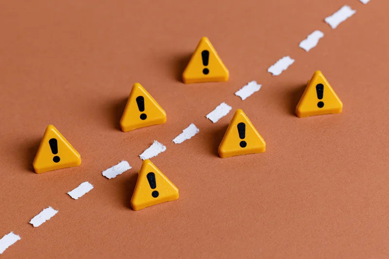 Yellow triangular warning signs with exclamation marks arranged along a dashed white line on a brown surface