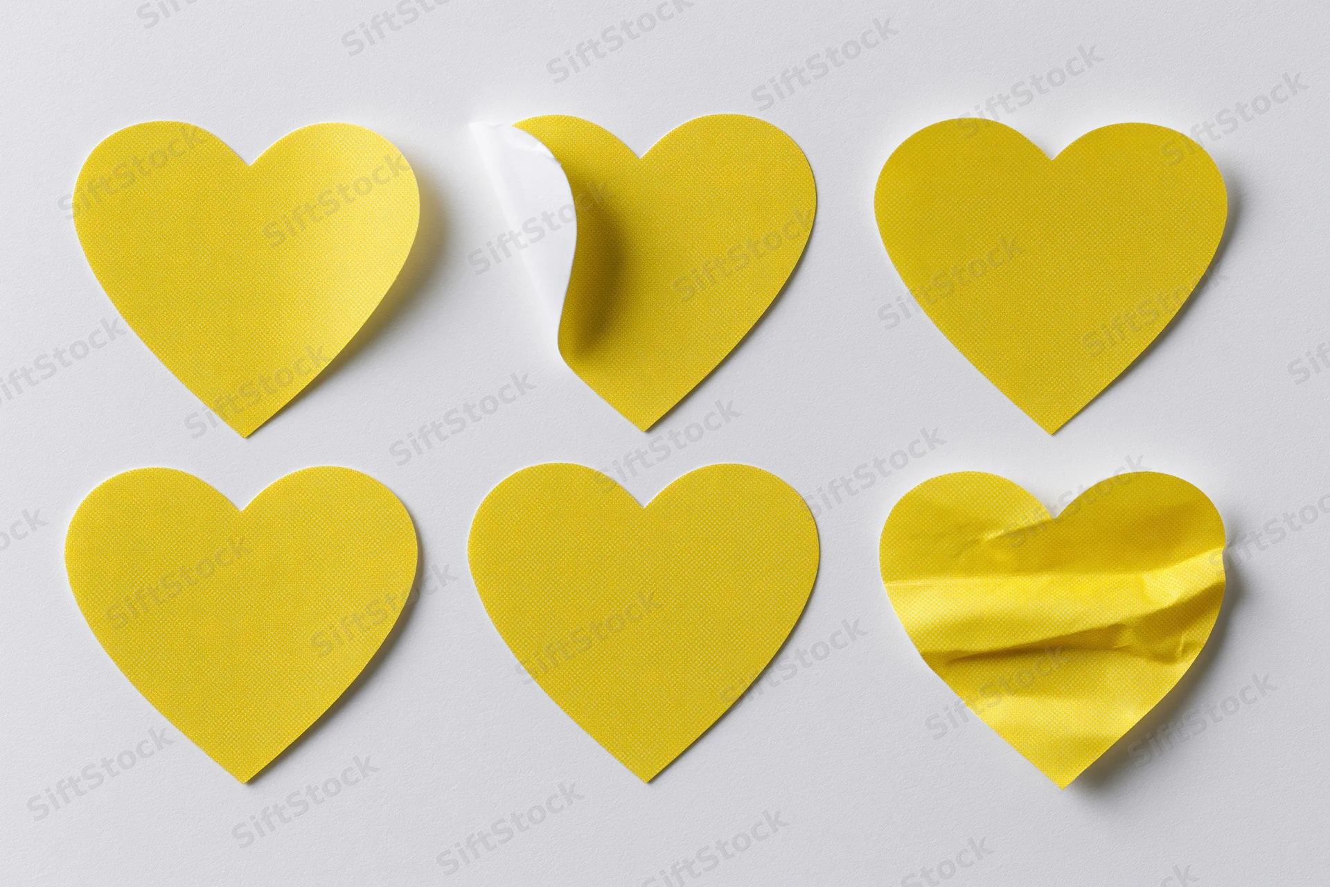 Six yellow heart-shaped stickers arranged in two rows on a white surface