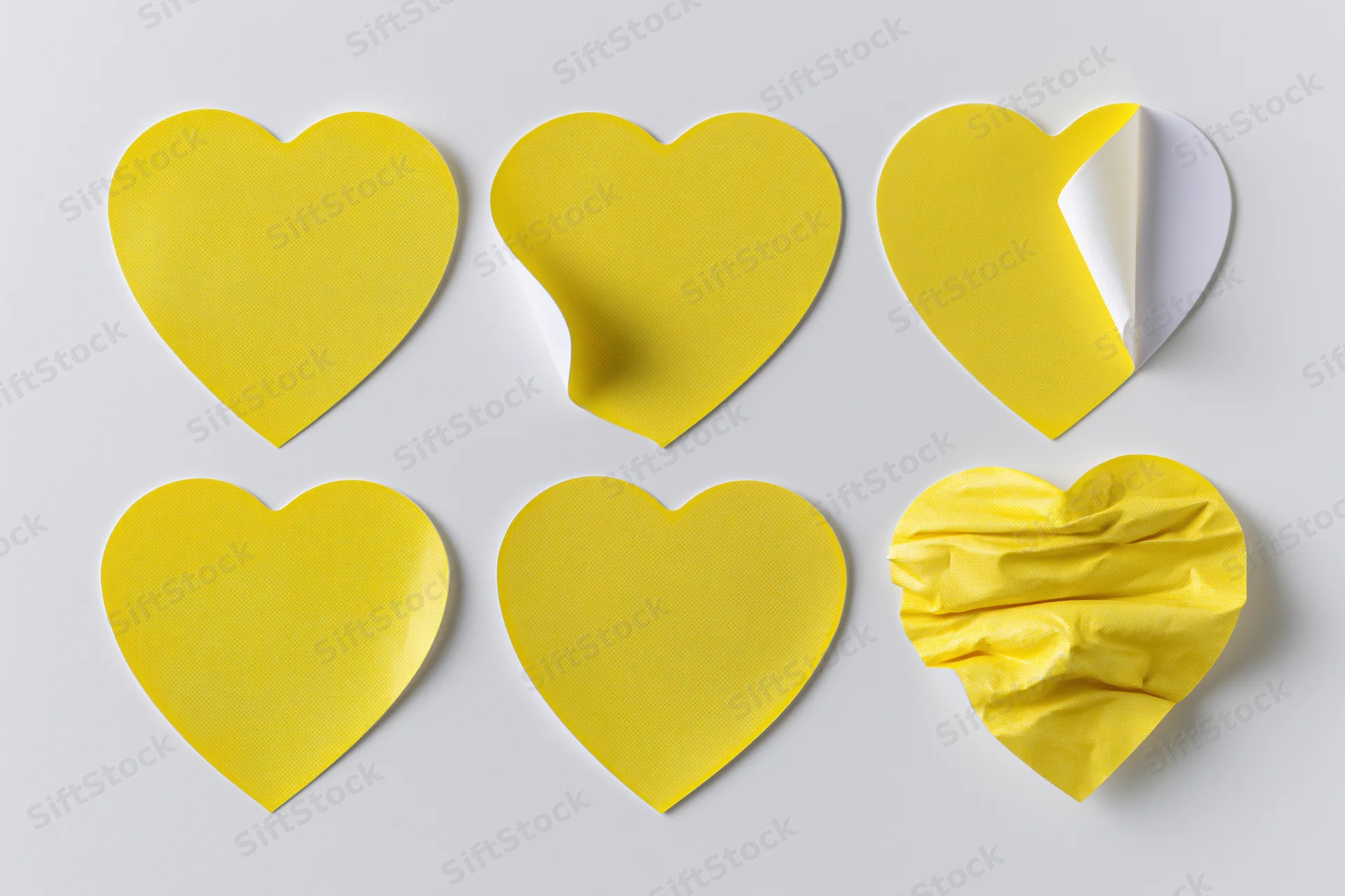 Six yellow heart-shaped stickers arranged in two rows on a white surface, one peeled and one crumpled